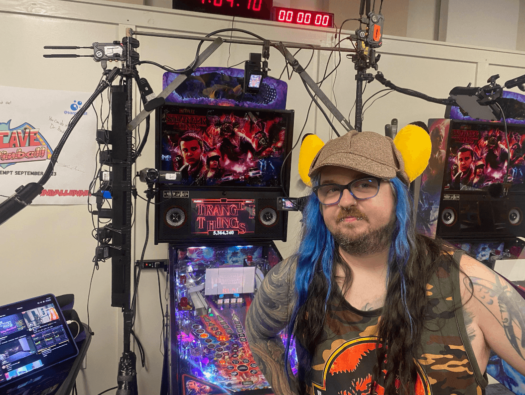 Stranger Things pinball machine with colorful display and person wearing yellow ear muffs
