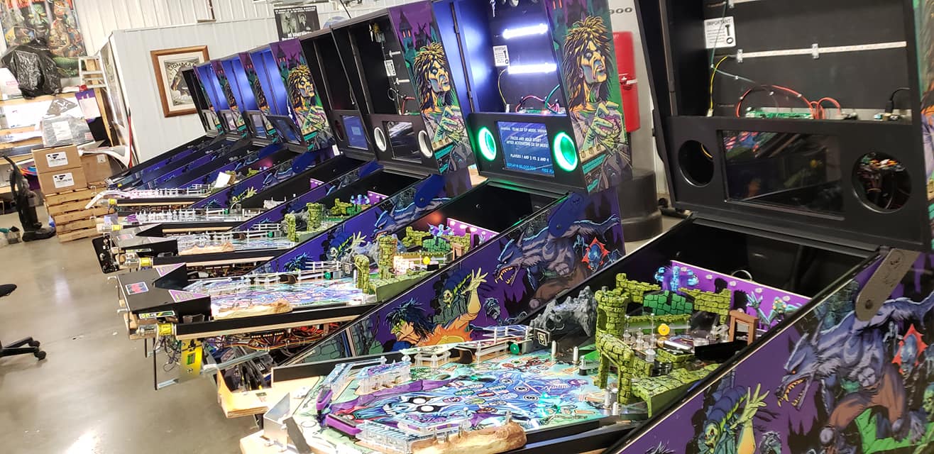 Multiple colorful pinball machines with fantasy-themed artwork in warehouse