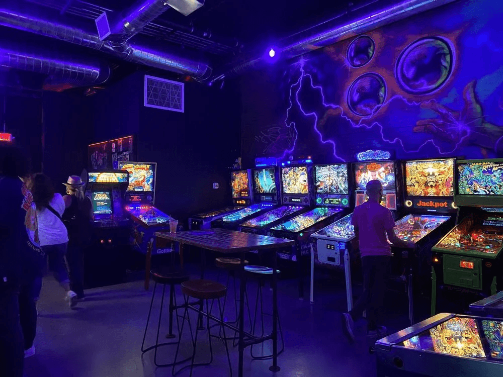 Dimly lit arcade with colorful pinball machines under blue neon lighting