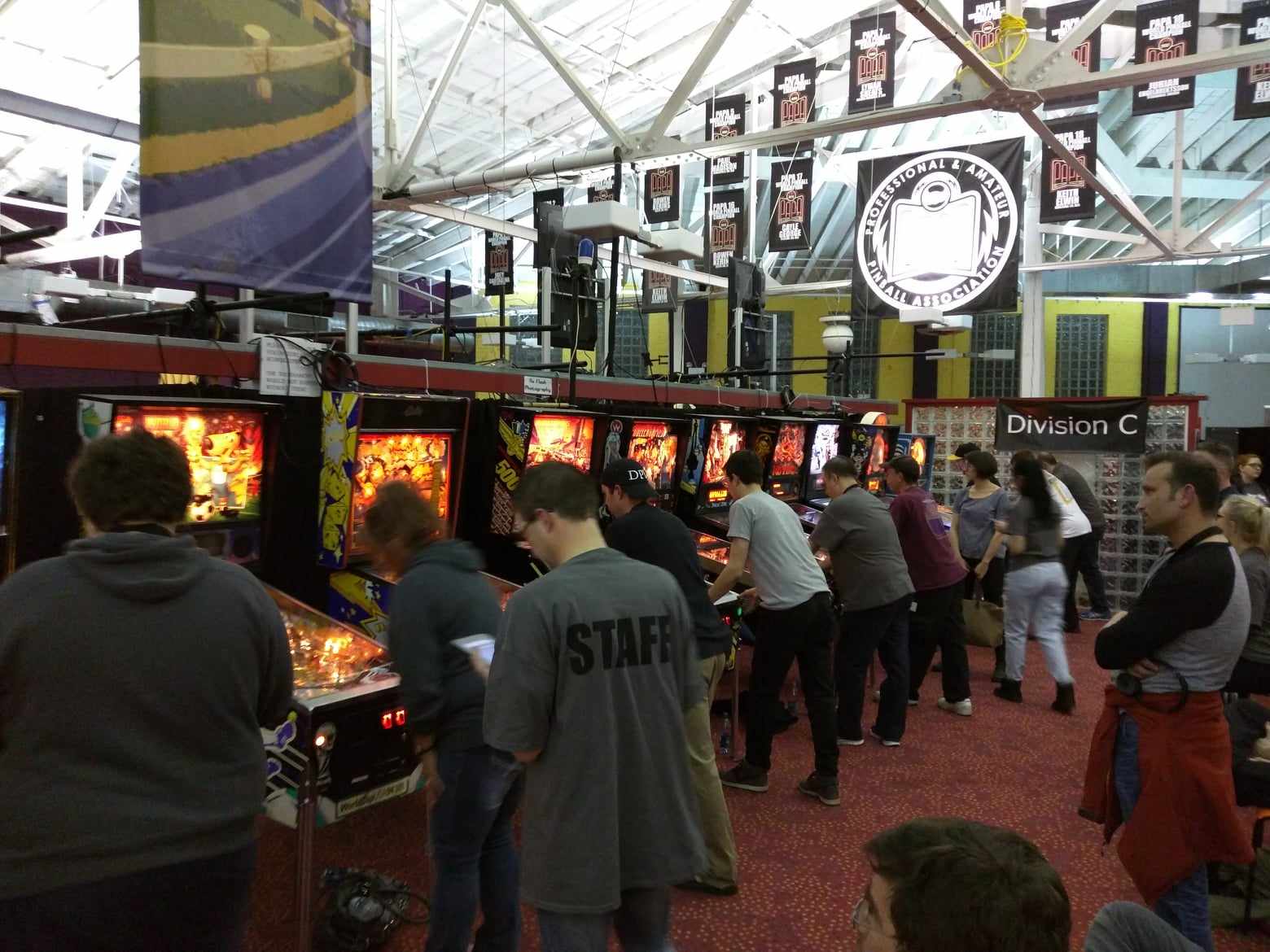 Crowded pinball tournament with players competing at illuminated machines