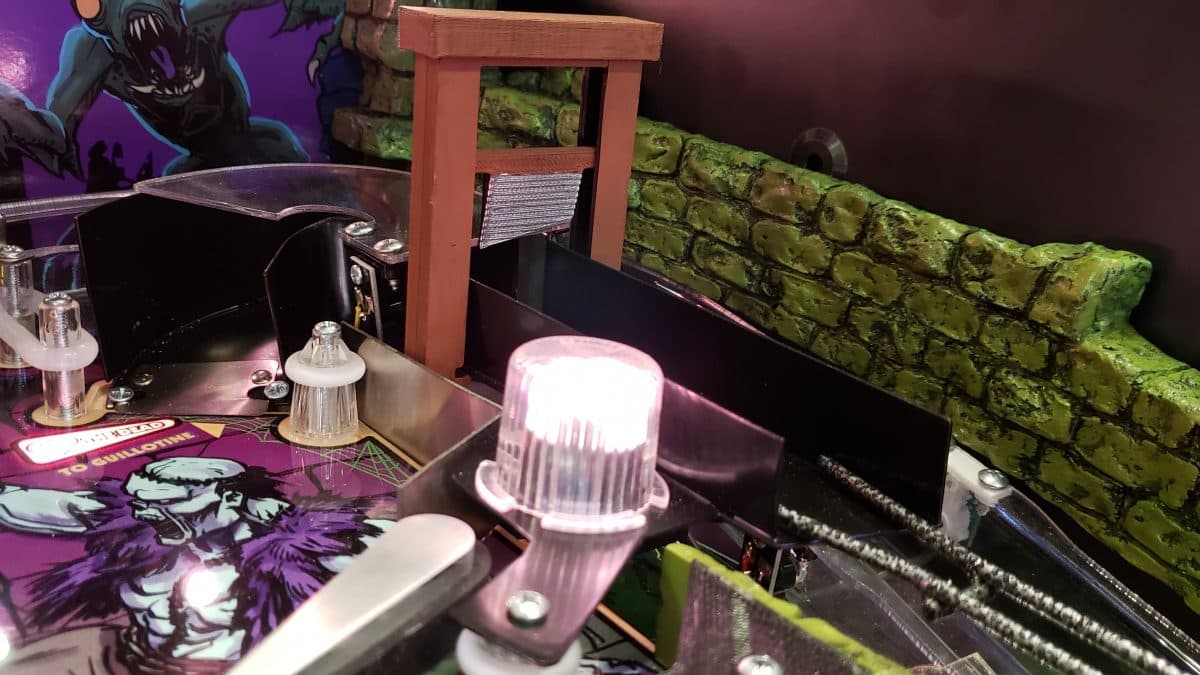 Pinball machine with glowing light, monster artwork, and green stone wall