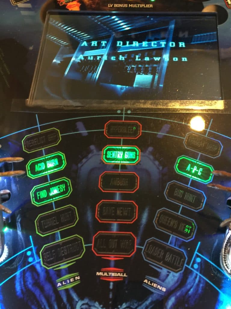 Alien-themed pinball machine with glowing neon green and red buttons