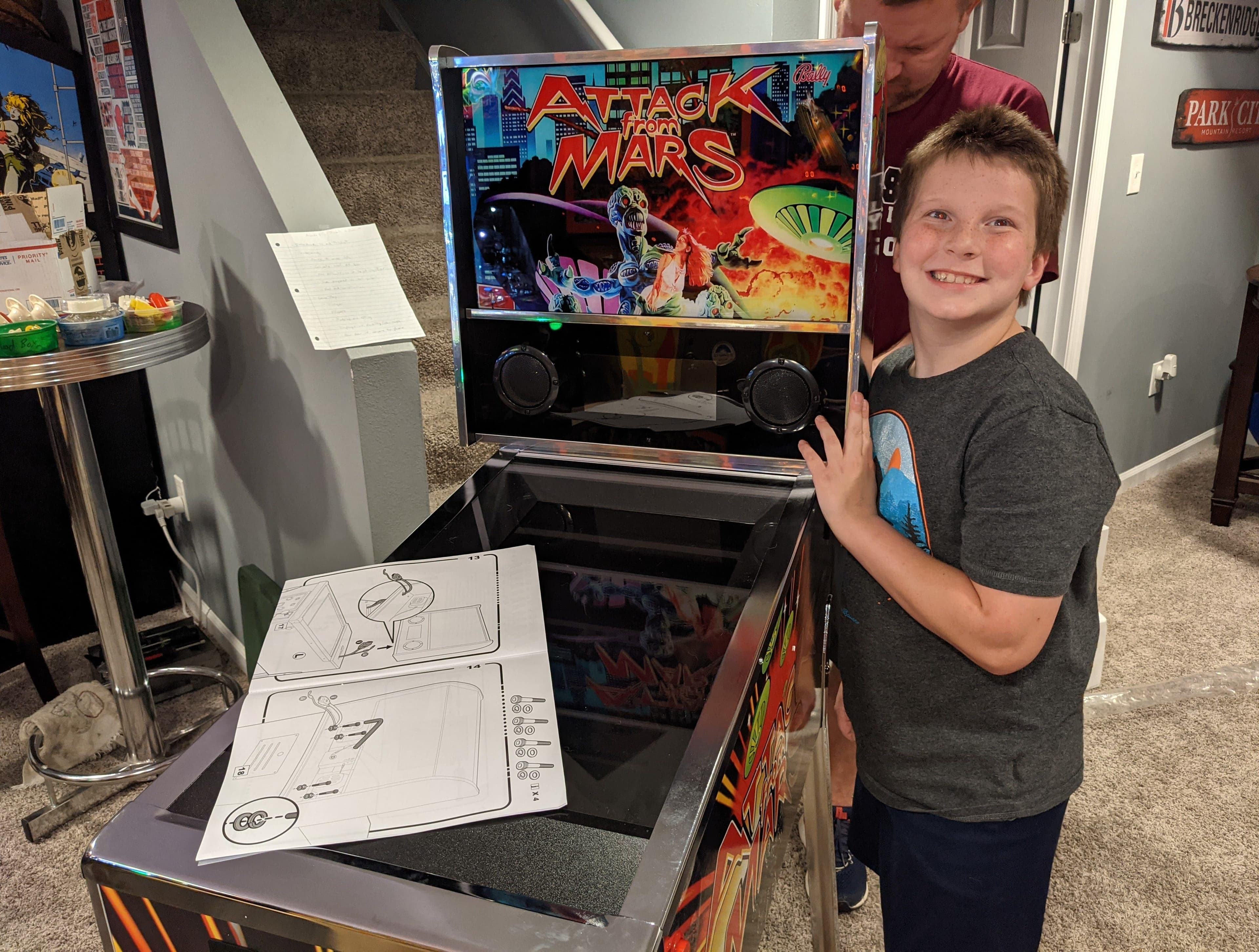 Smiling child standing next to Attack from Mars pinball machine