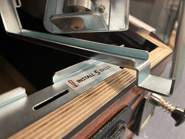 Close-up of a machine with "Install 5 balls" label on a metal surface