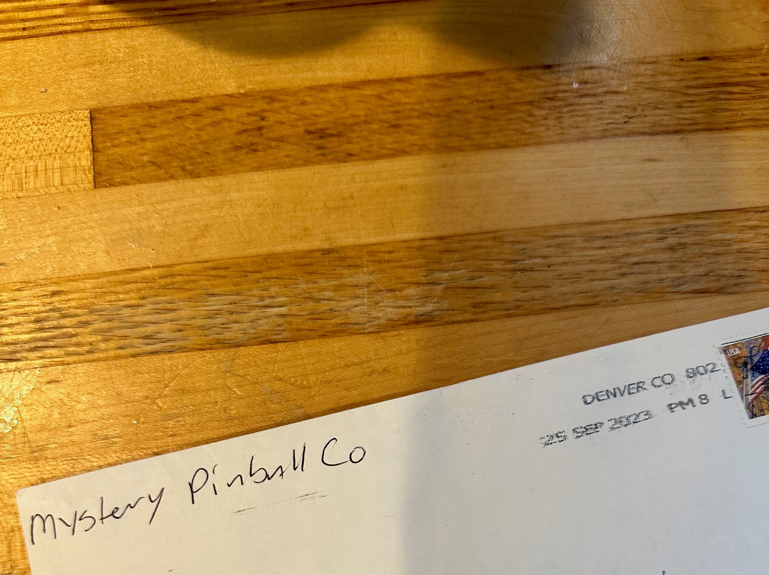 Envelope with "Mystery Pinball Co" handwritten on wooden surface