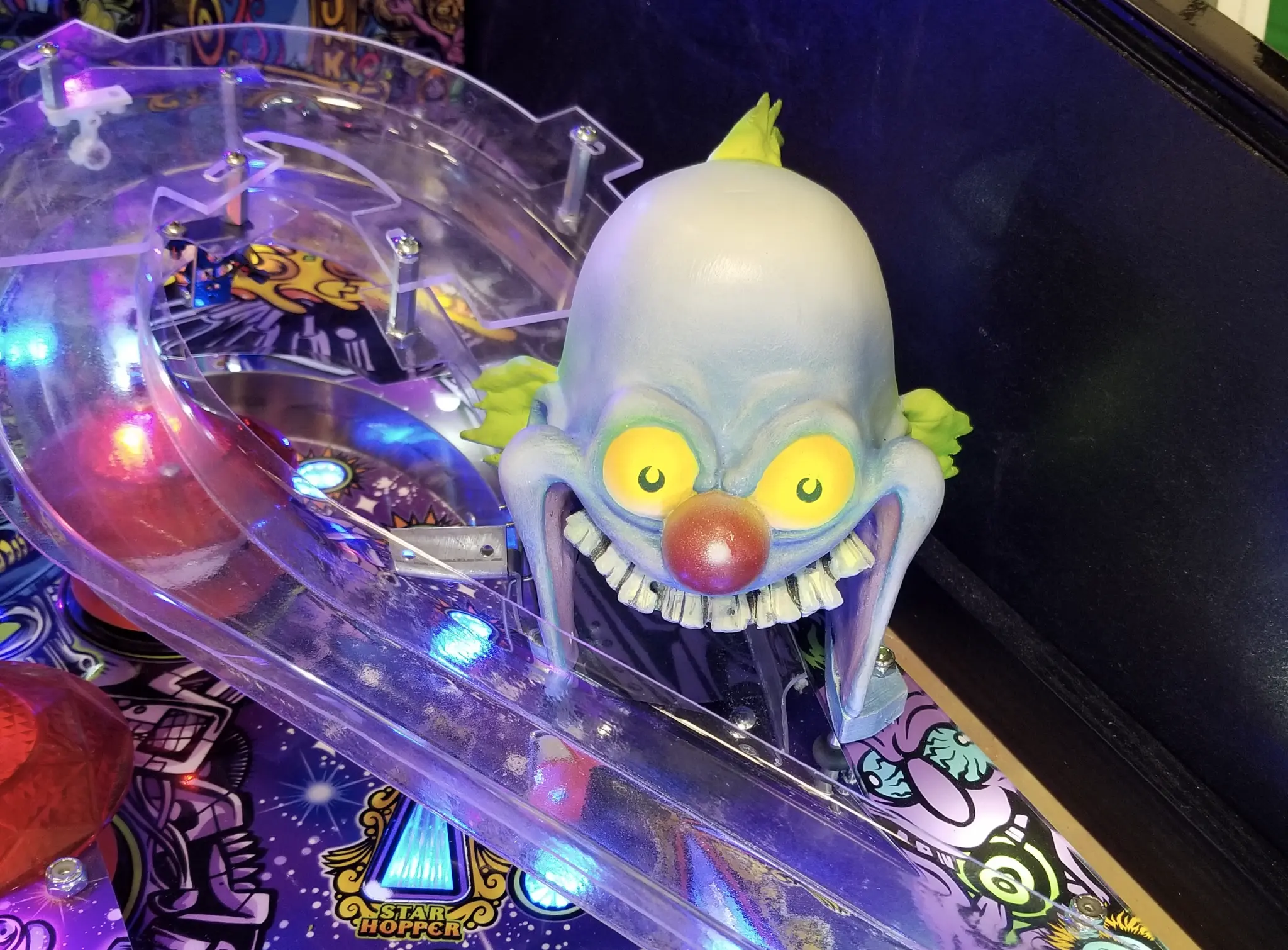 Creepy clown head on colorful pinball machine with glowing lights