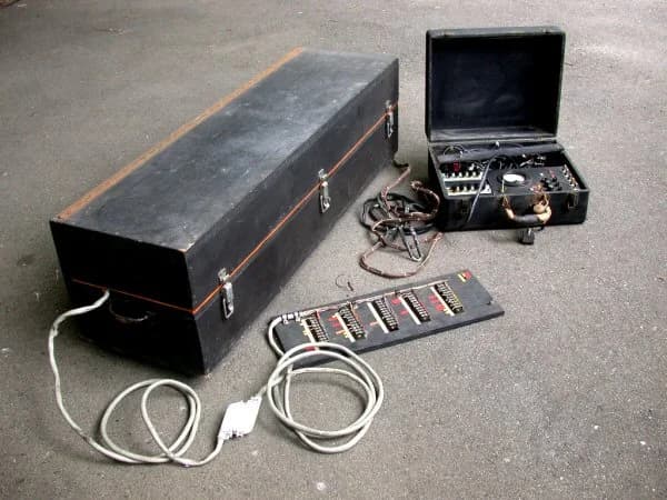 Vintage electronic equipment with cases, cables, and control panels on concrete