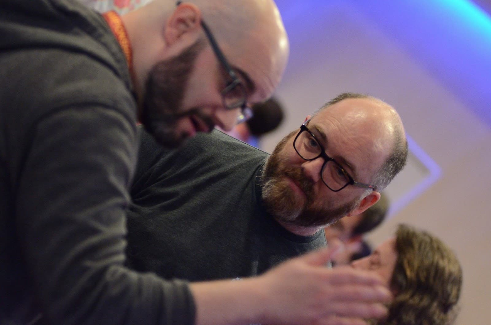 Bearded man with glasses interacting with another person in blue-lit setting
