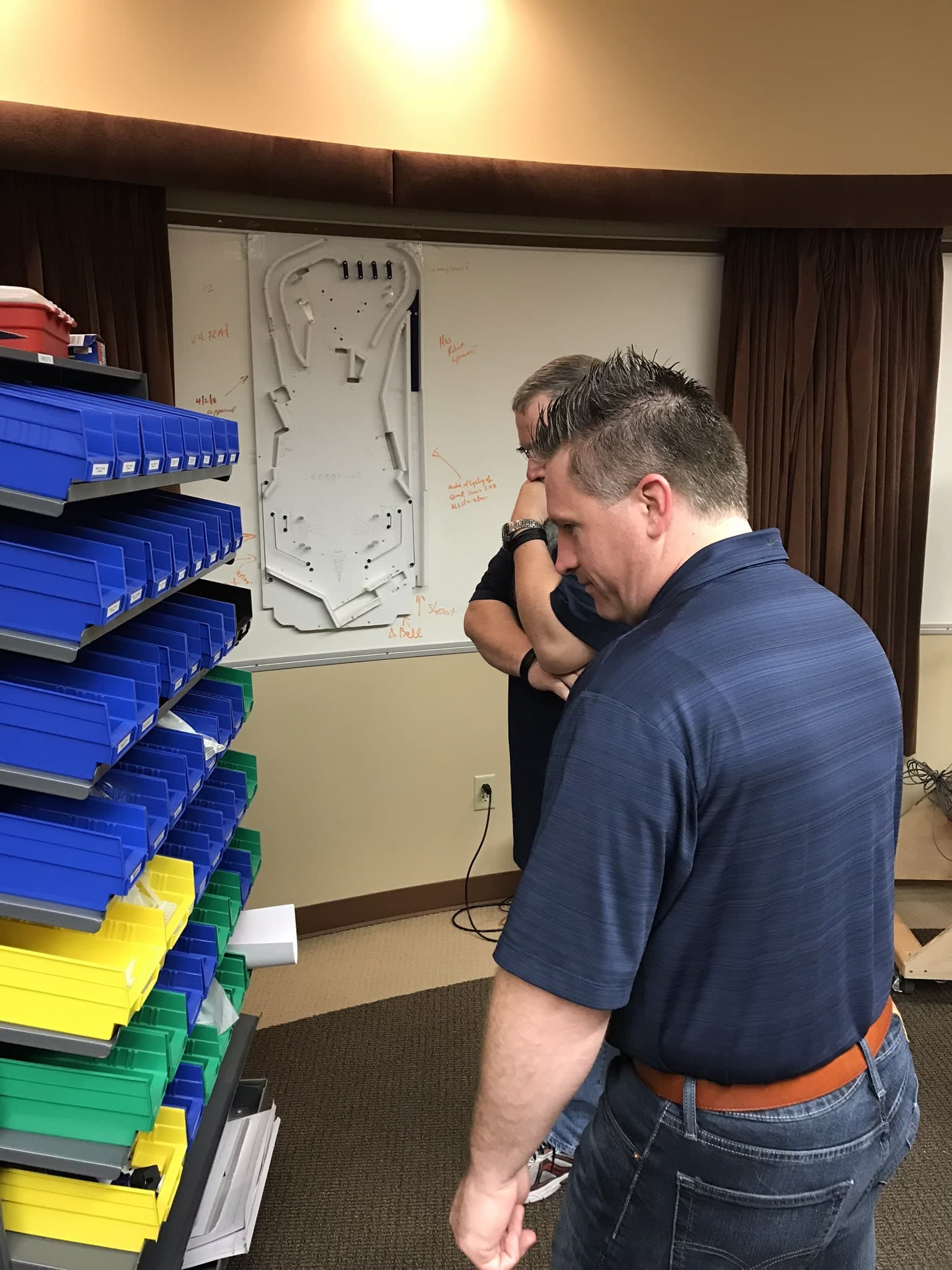 Two people analyzing blueprint of mechanical design near colorful storage shelves