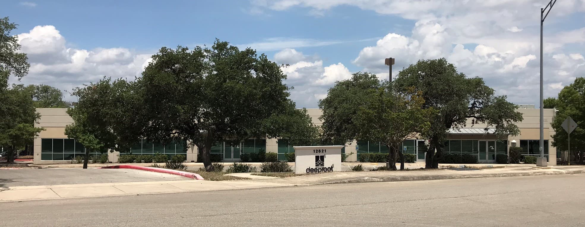 Deeproot office building with trees and parking lot on sunny day