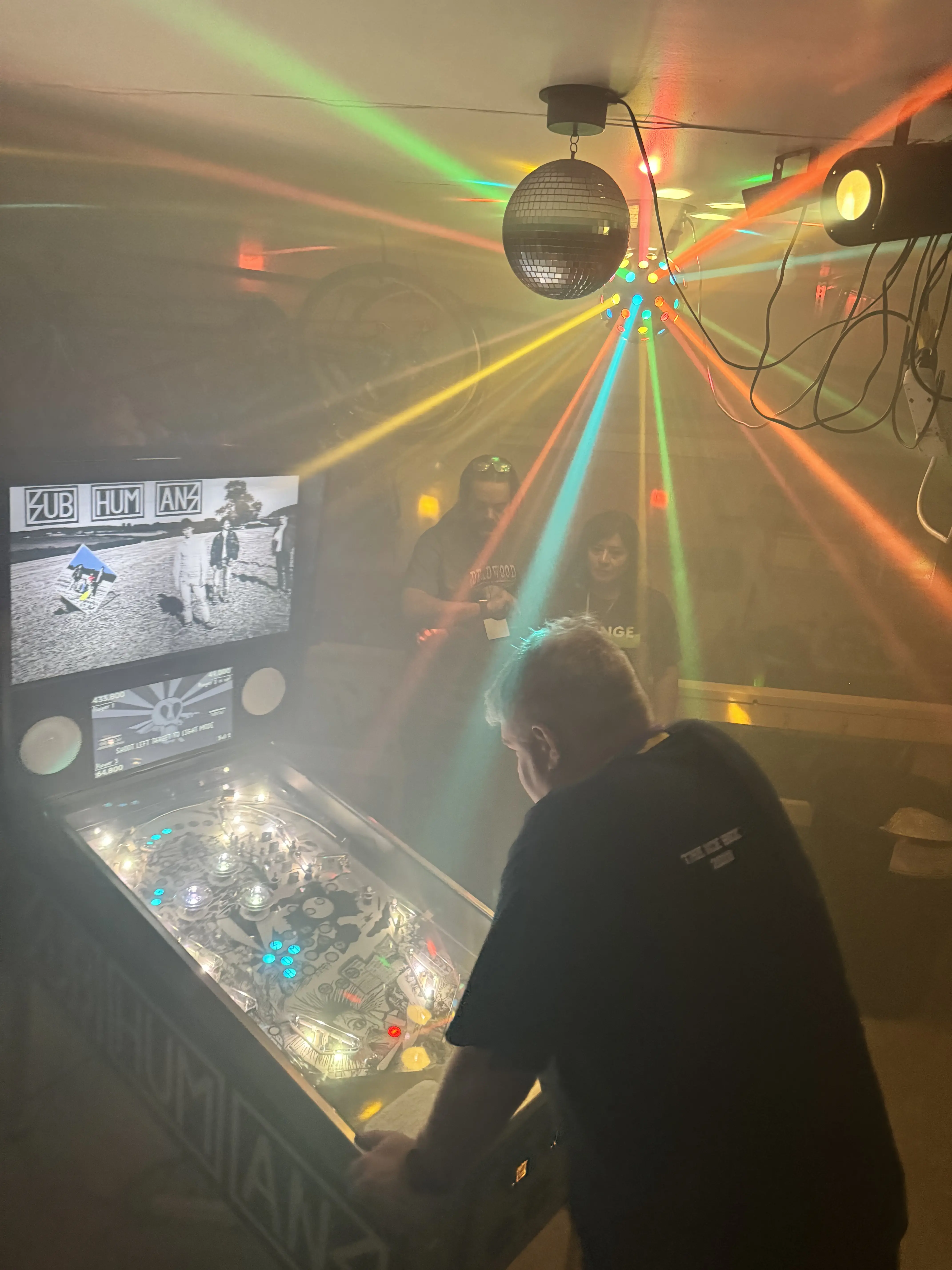 Pinball machine under colorful disco ball lights in dimly lit room