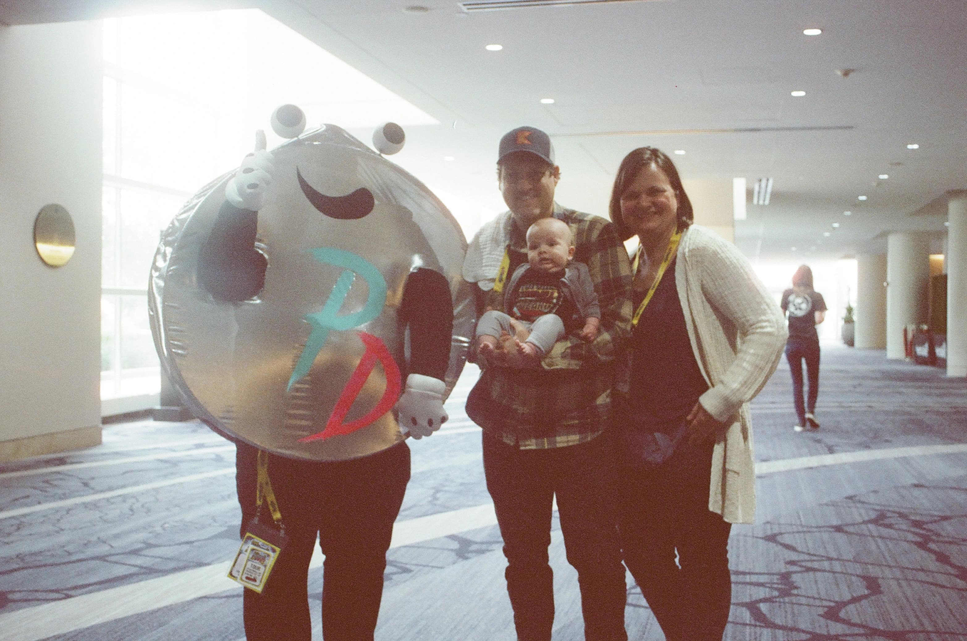 People posing with mascot and baby in conference hallway