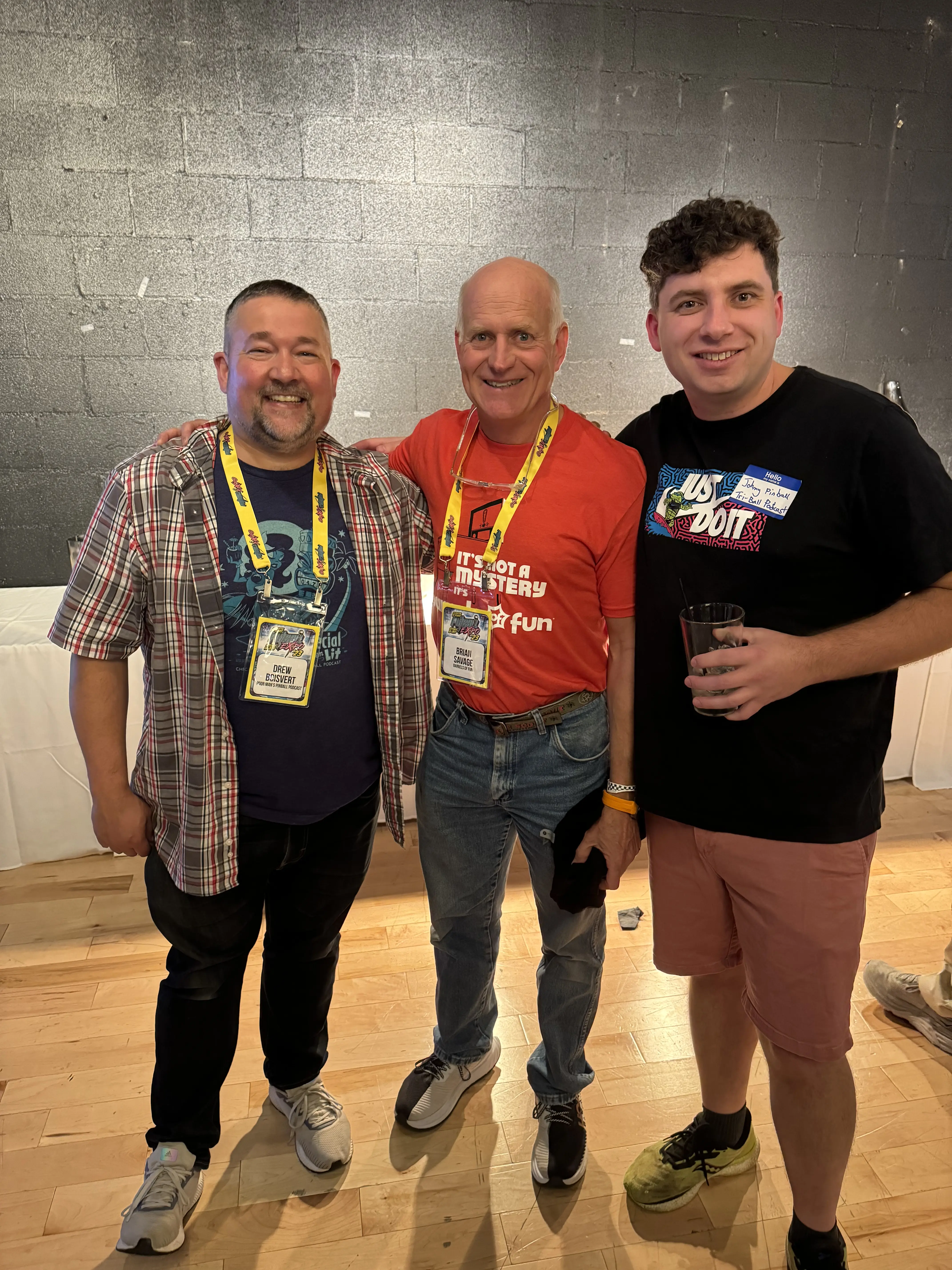 Three men smiling together at an event, wearing name tags and lanyards