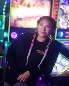 Smiling person with braids standing near colorful arcade game machines