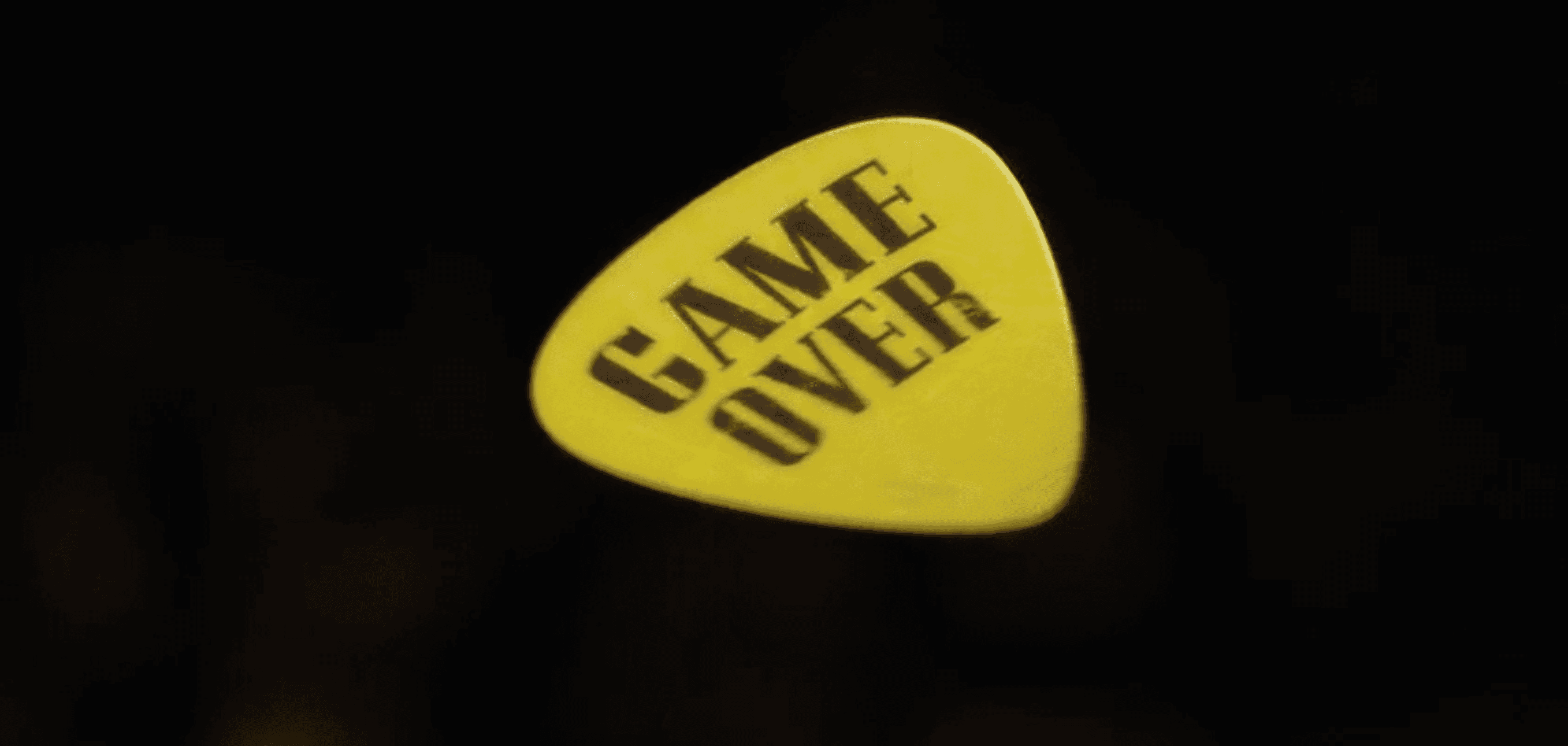 Yellow guitar pick with Game Over text on black background