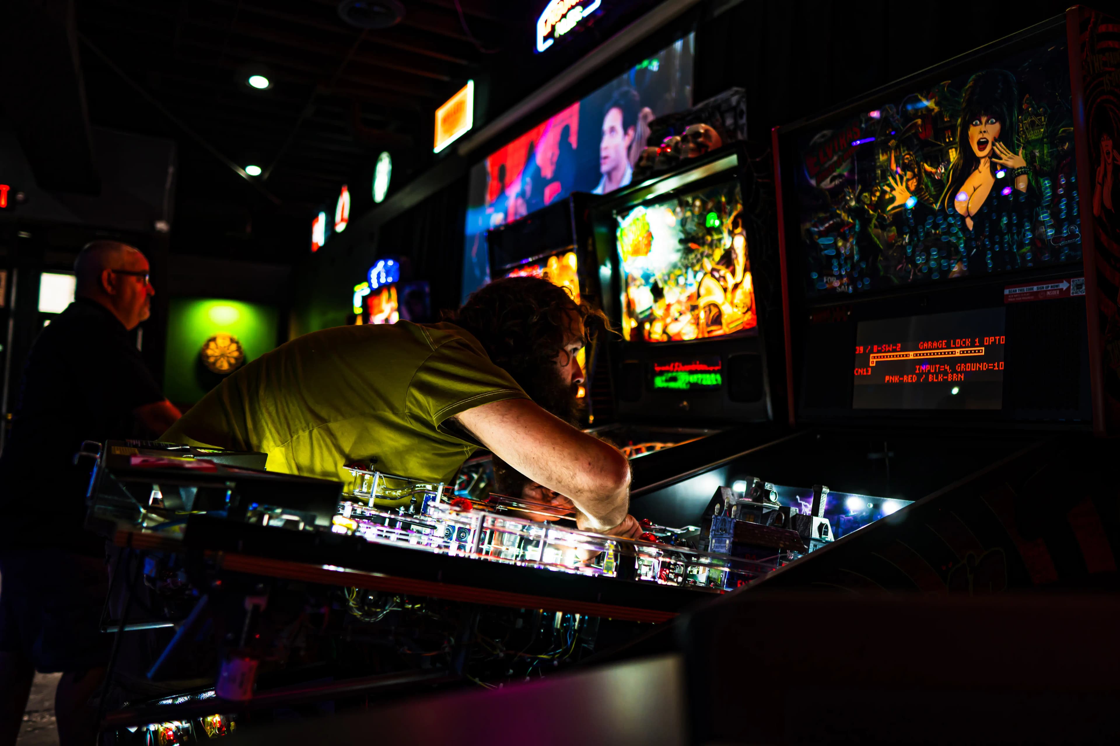 Pinball player intensely focused on illuminated machine in dark arcade
