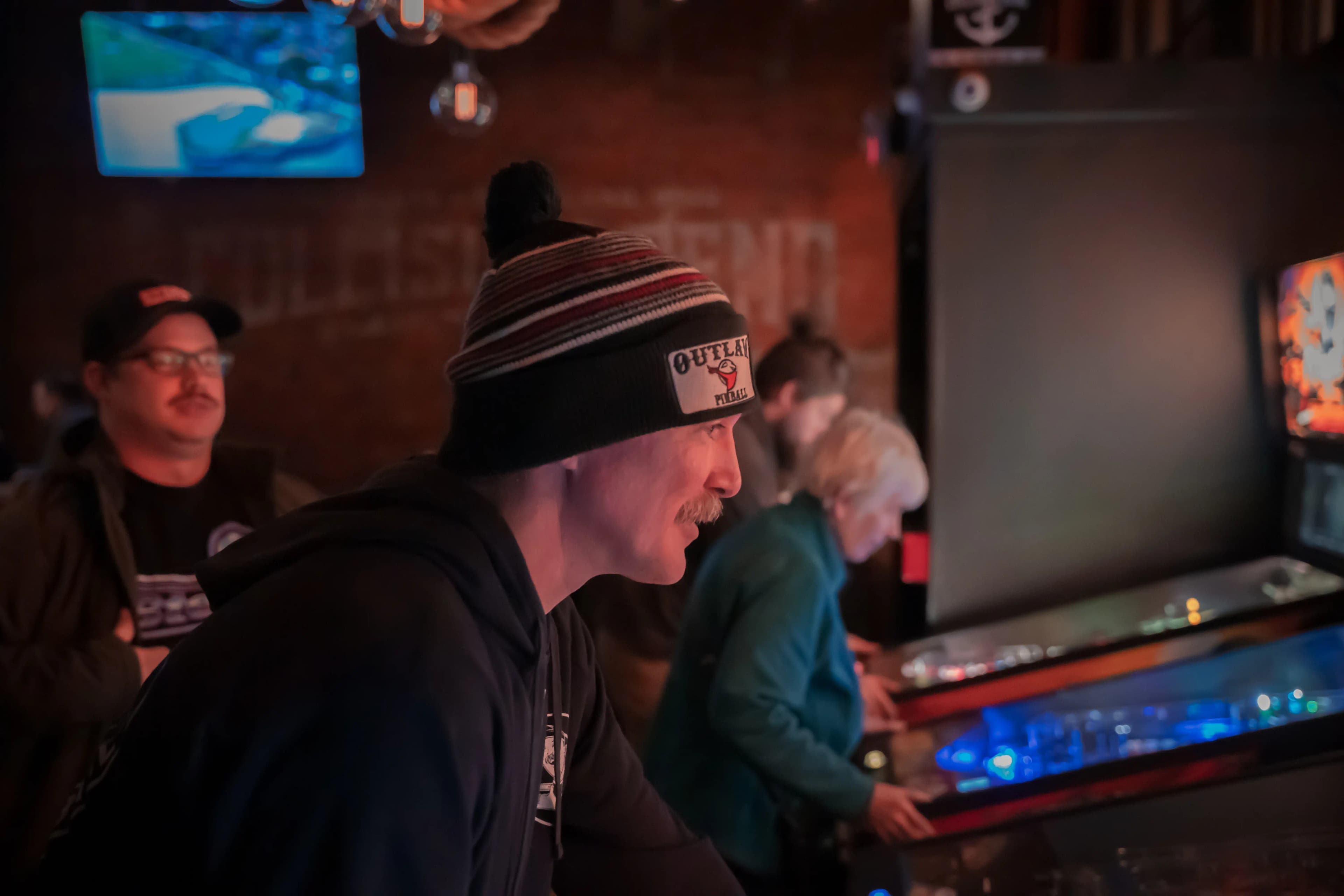 Pinball player in Outlaw hat concentrates intently during competitive game