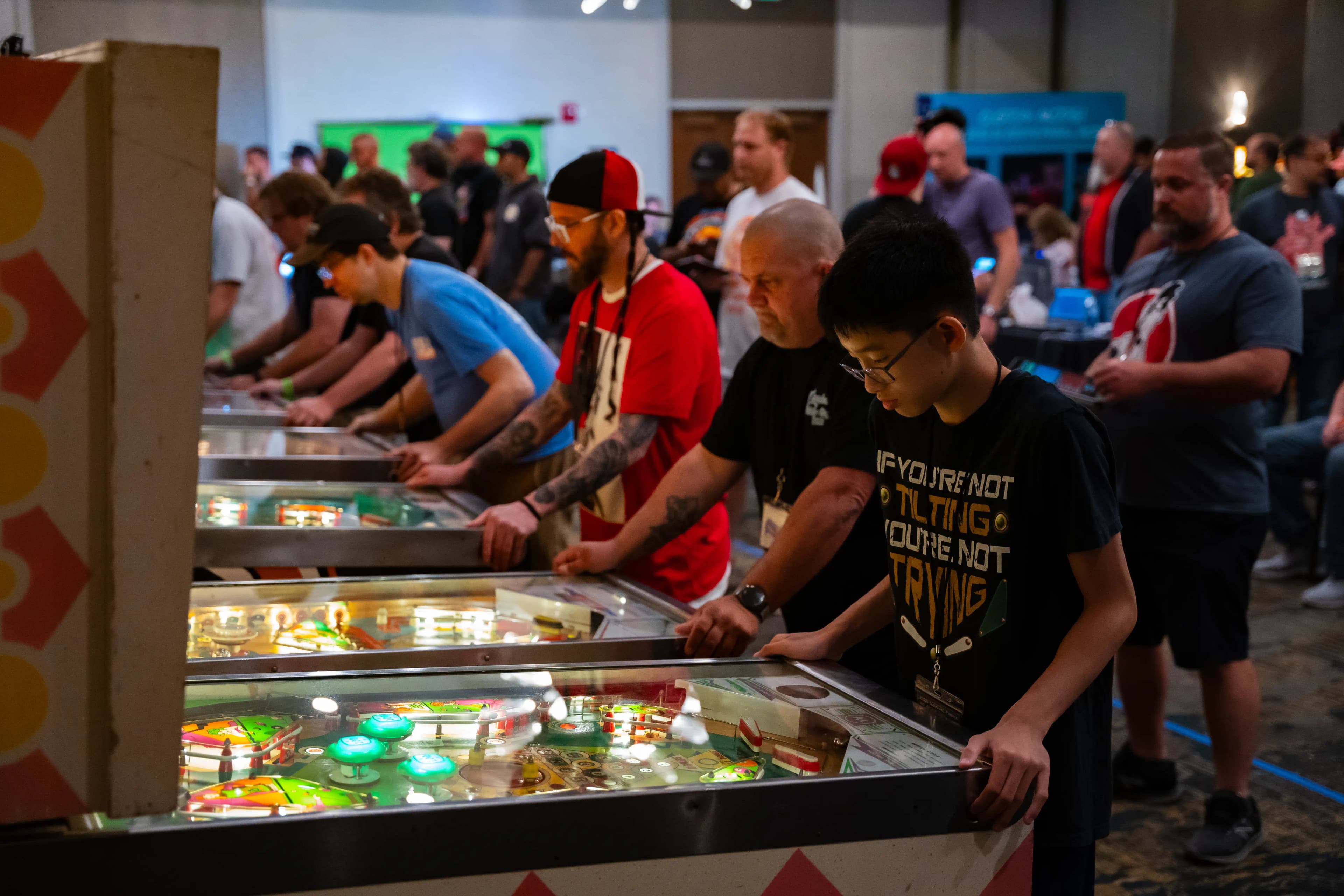 People playing pinball machines at a crowded arcade or gaming event