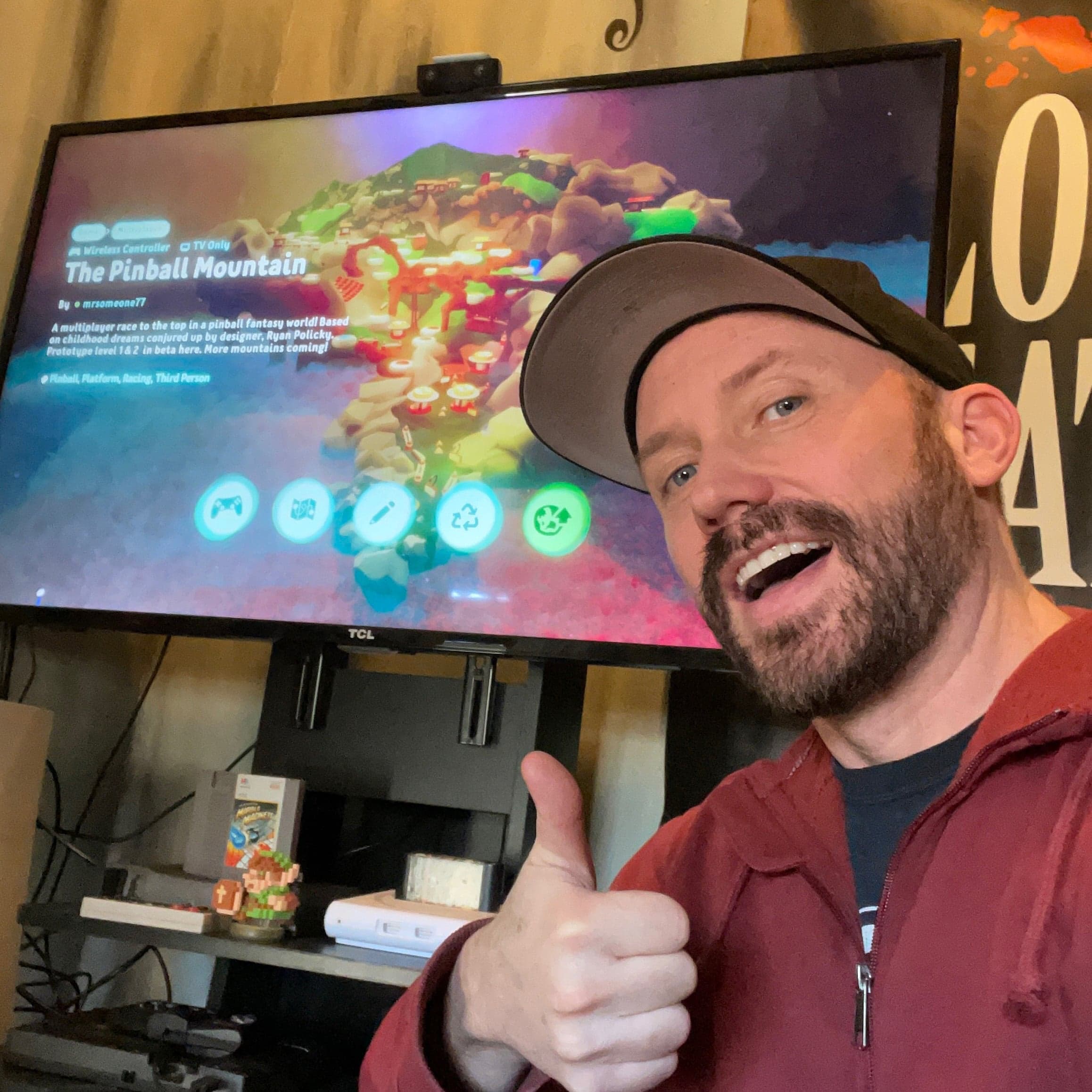 Gamer giving thumbs up next to screen showing Pinball Mountain video game