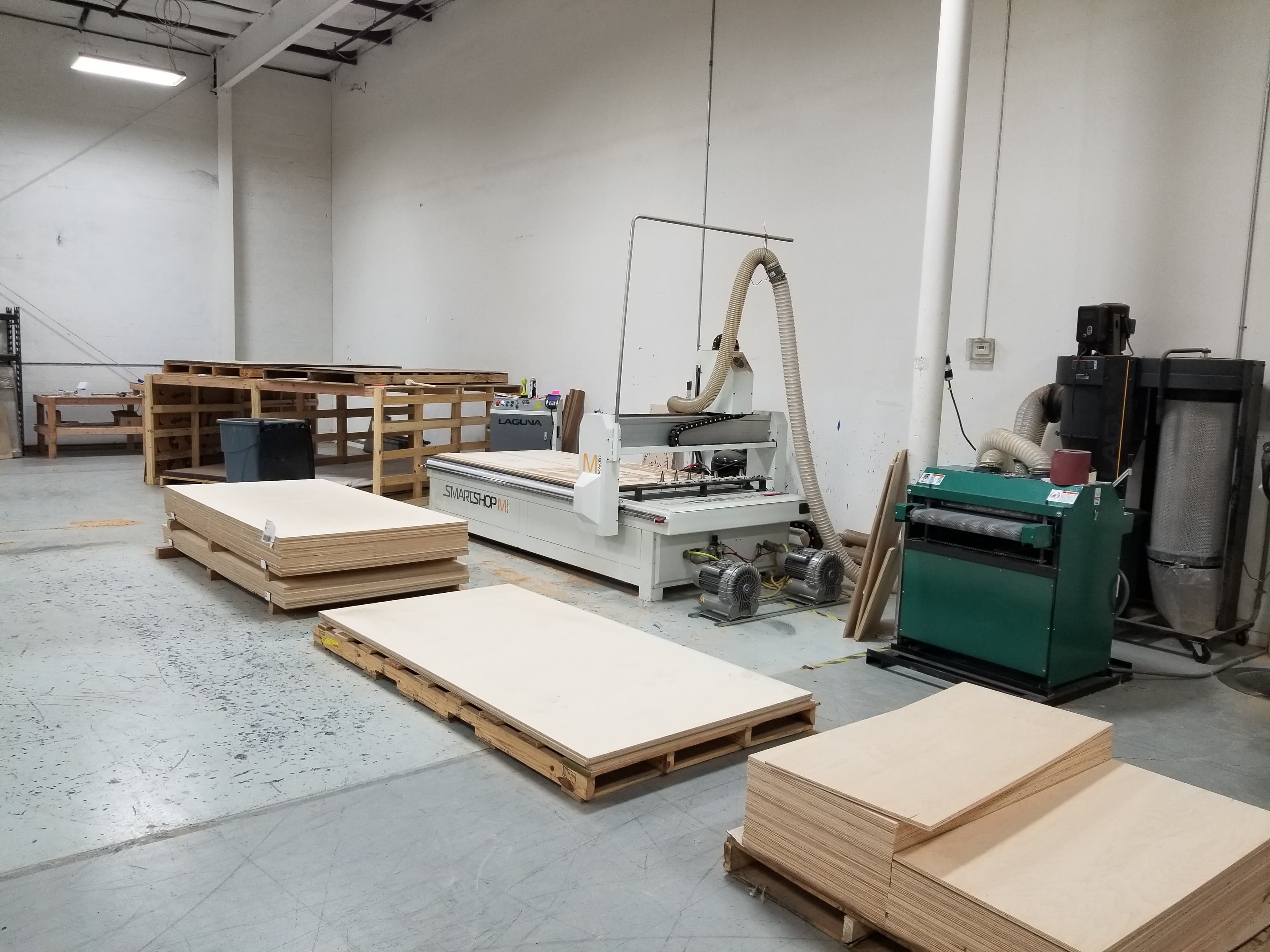 Woodworking workshop with CNC machine, wood sheets, and industrial equipment