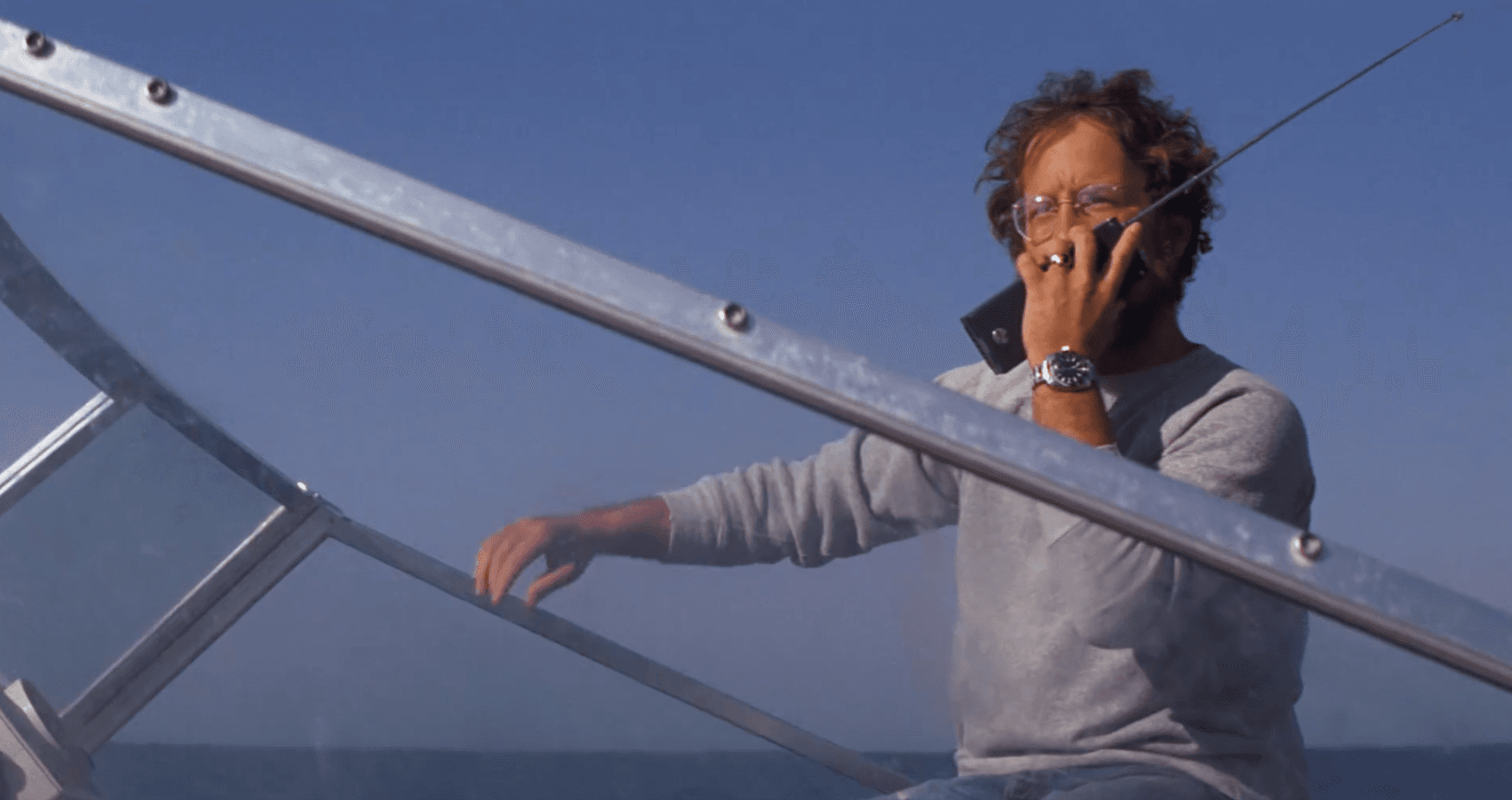 Person talking on phone on boat deck with blue sky and ocean background