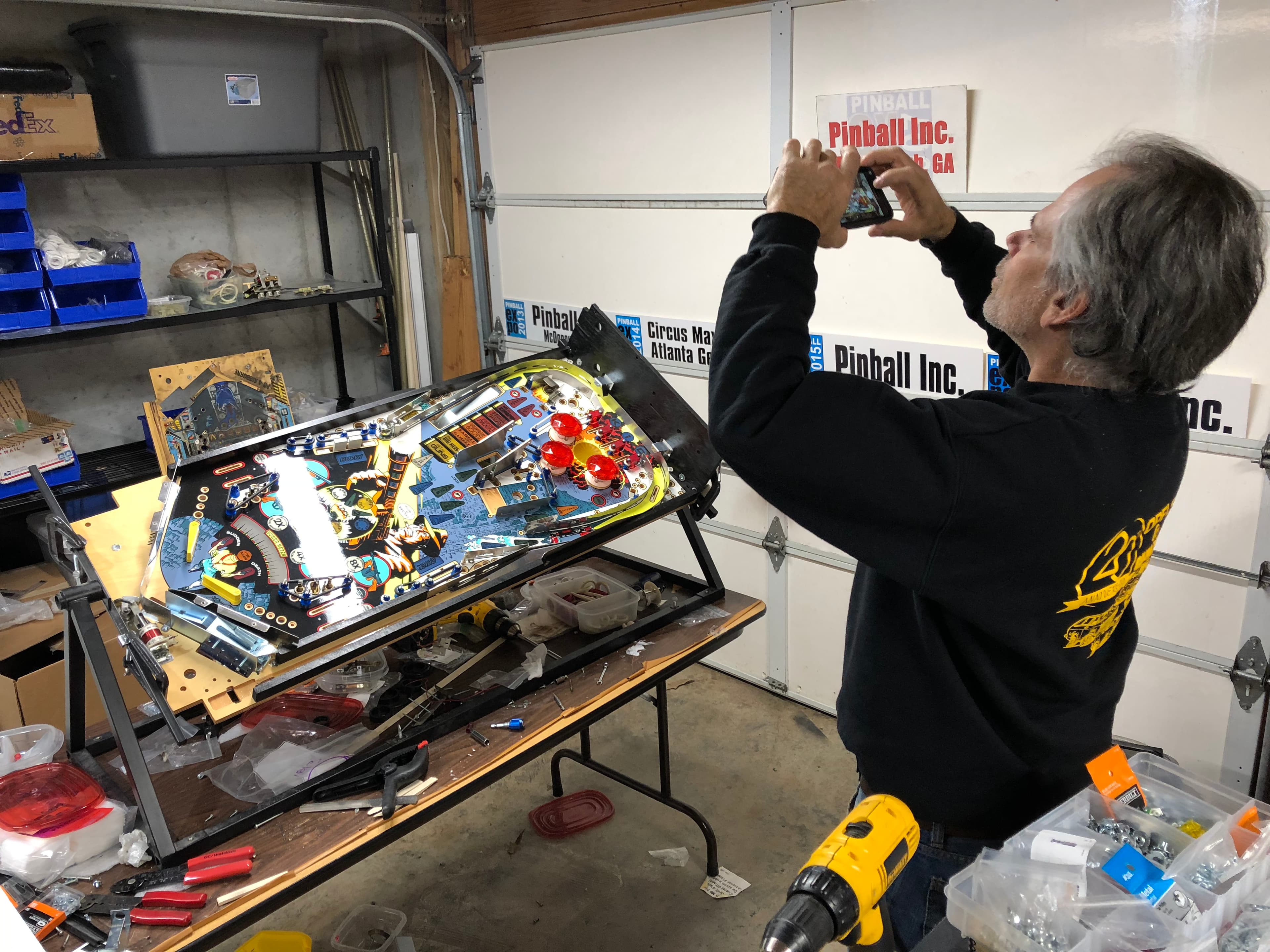 Technician photographing pinball machine during repair in workshop