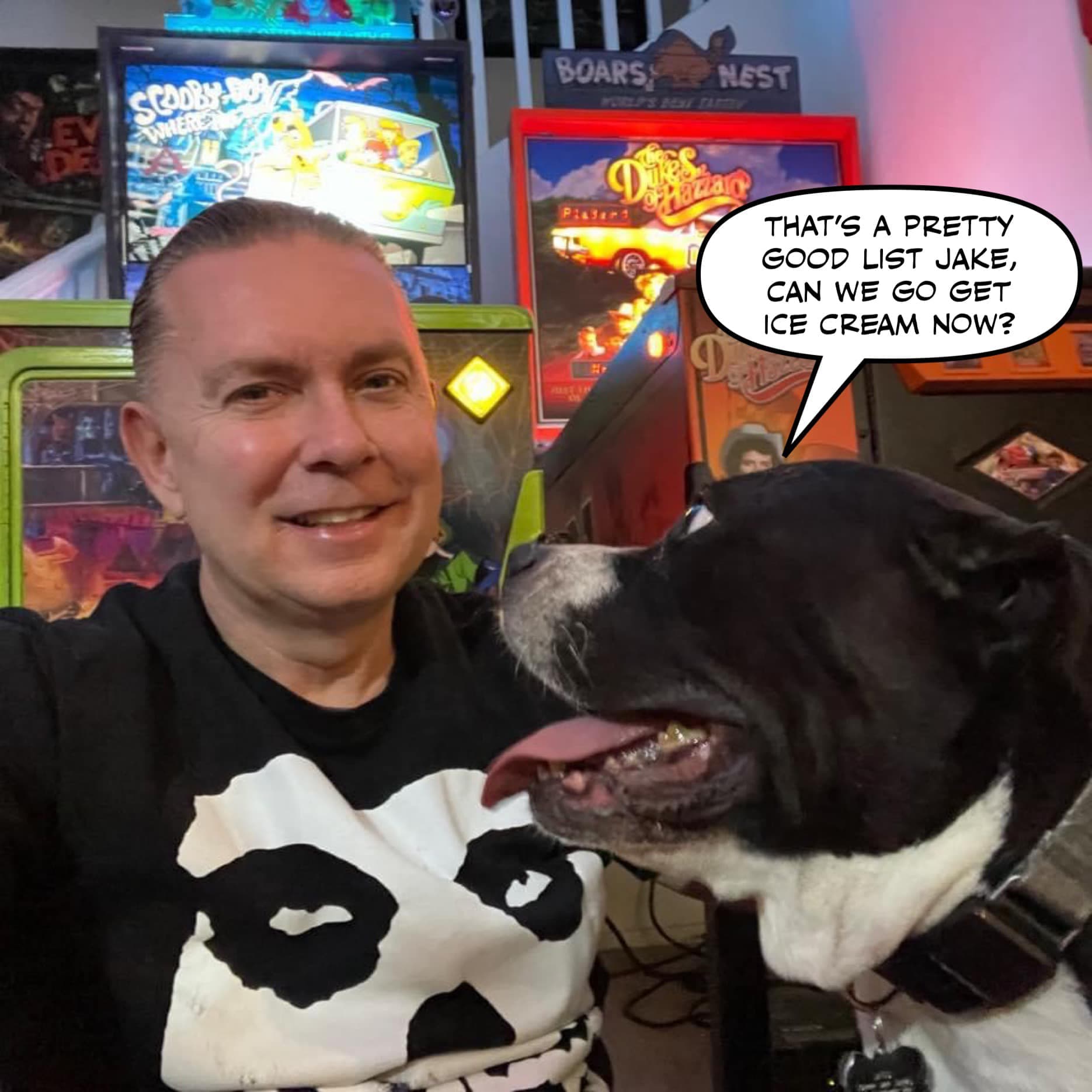 Smiling man with black and white dog in front of colorful game posters