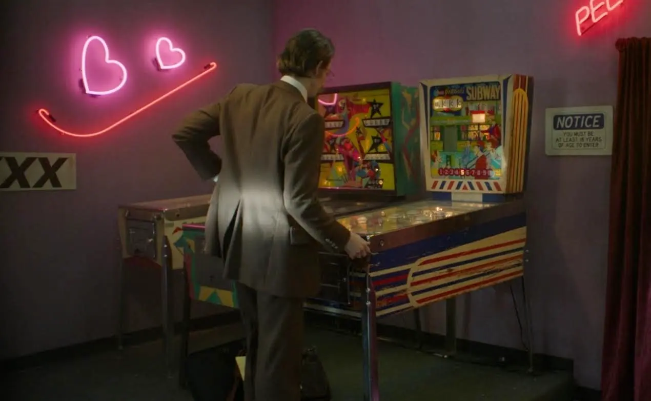 Person playing vintage pinball machine under neon hearts in dimly lit room