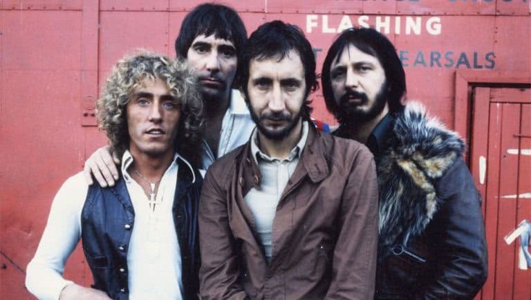 Four members of The Who band posing in front of a red background
