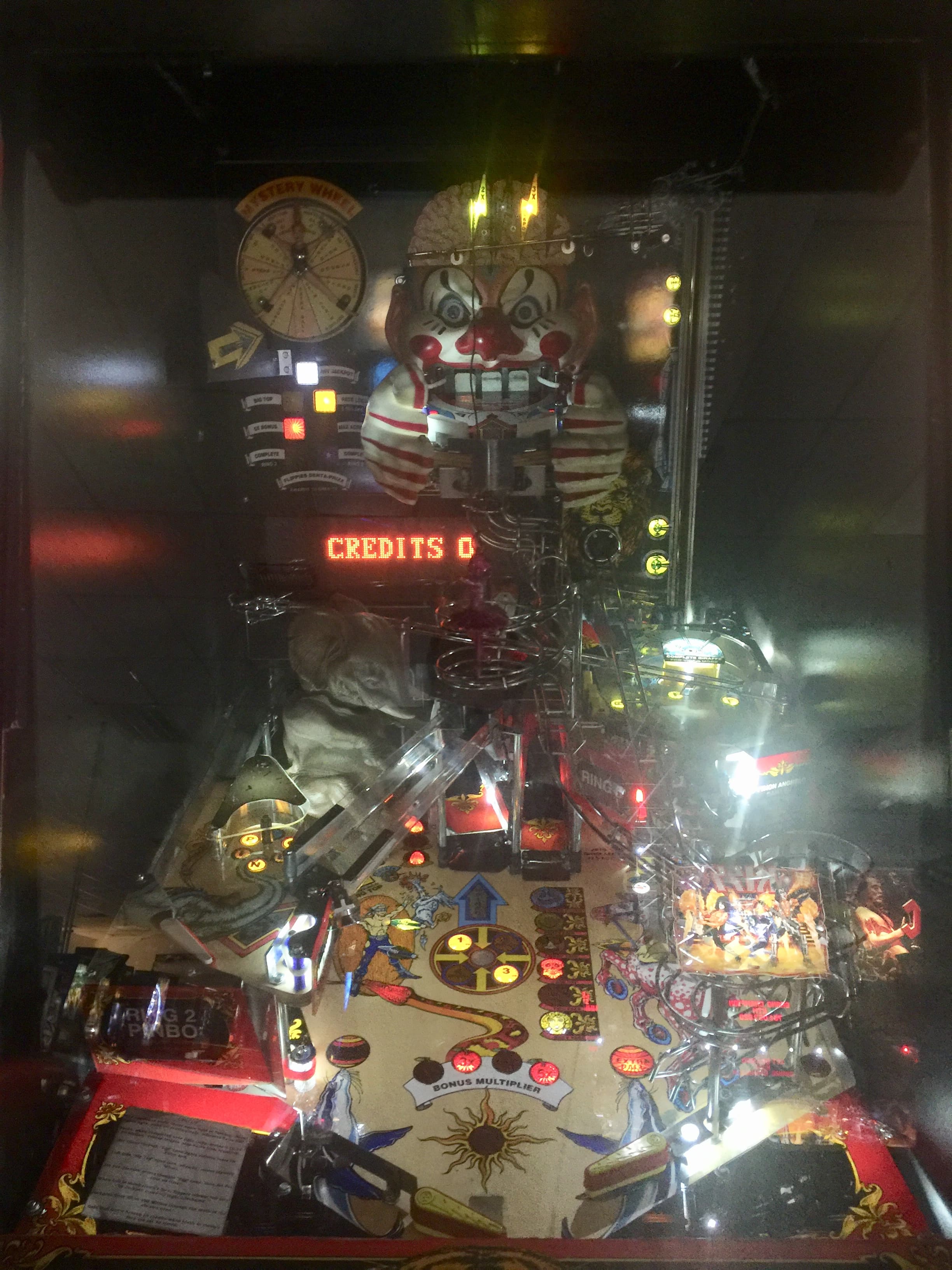 Vintage pinball machine with creepy clown backboard and illuminated gameplay