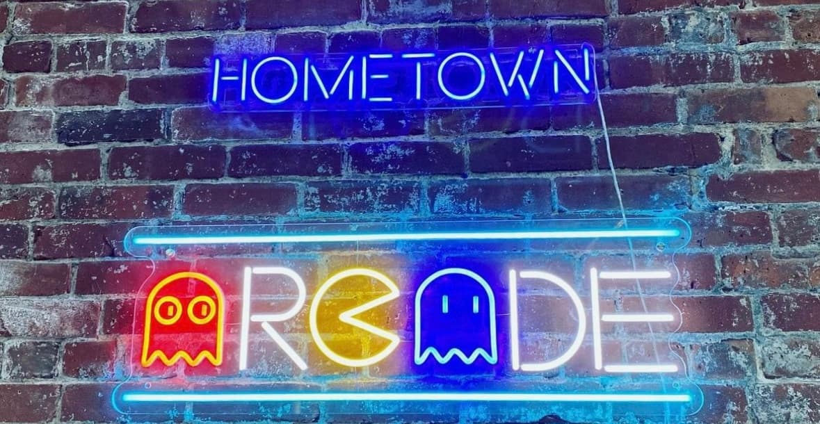Neon signs reading "Hometown Arcade" with Pac-Man ghosts on brick wall