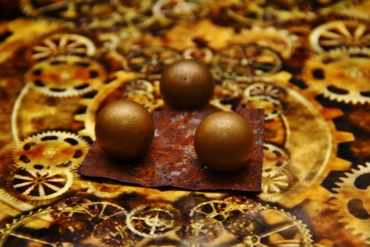Golden spheres on rusty metal plate surrounded by intricate mechanical gears
