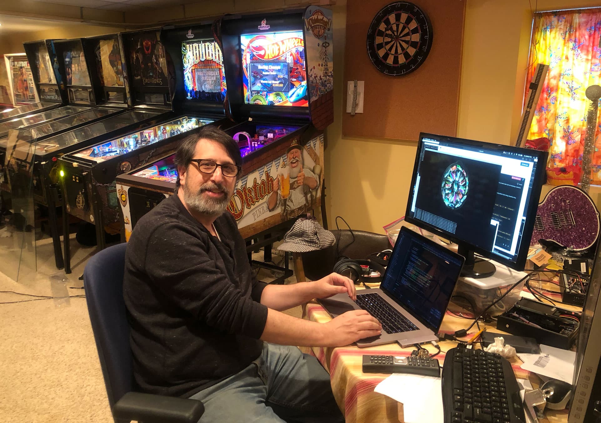 Man working at desk with pinball machines and dartboard in background