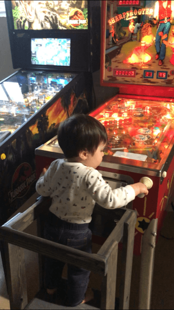Young child playing vintage pinball machine in arcade with colorful screens