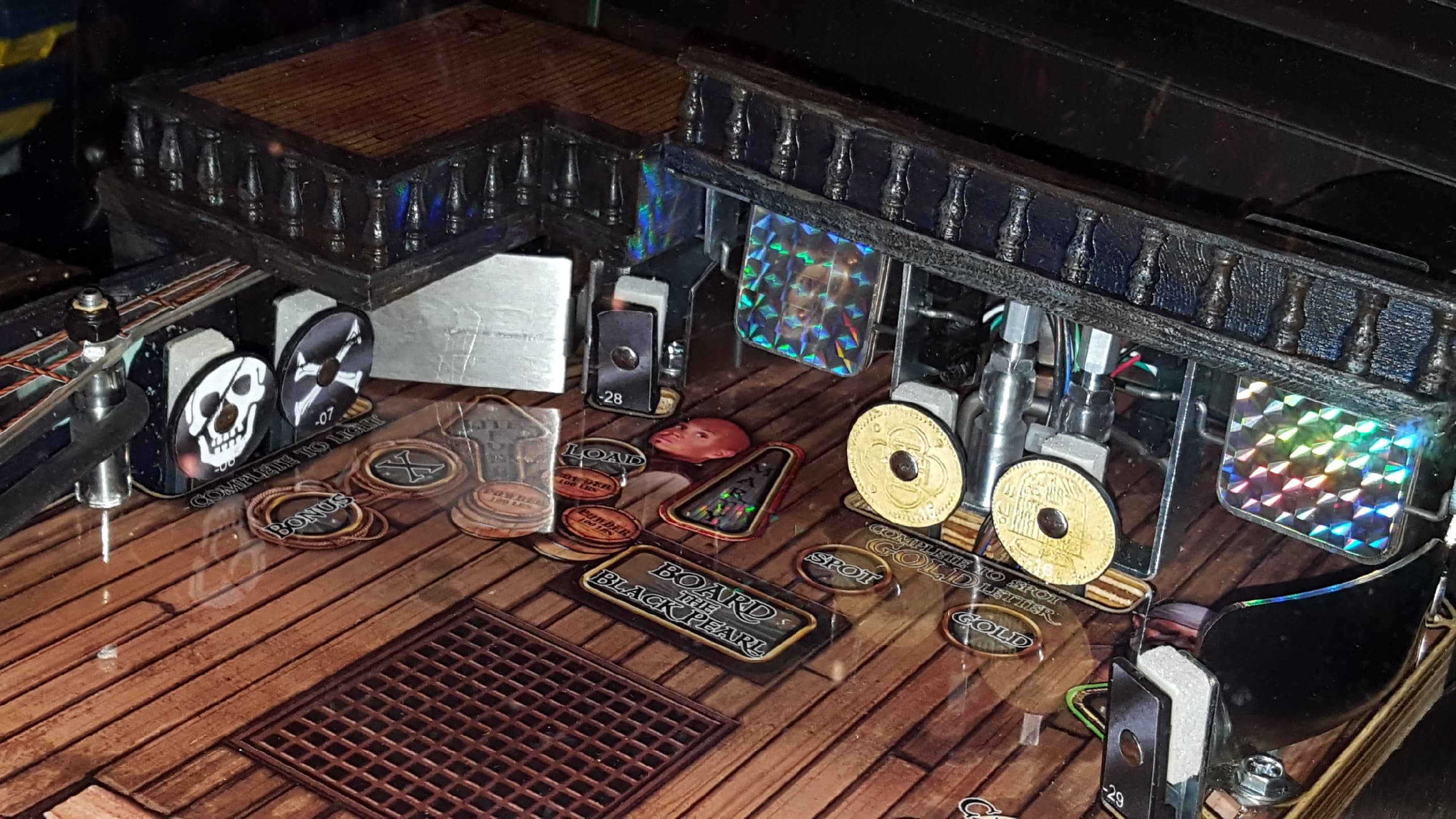 Board game components with tokens, coins, and skull marker on wooden surface