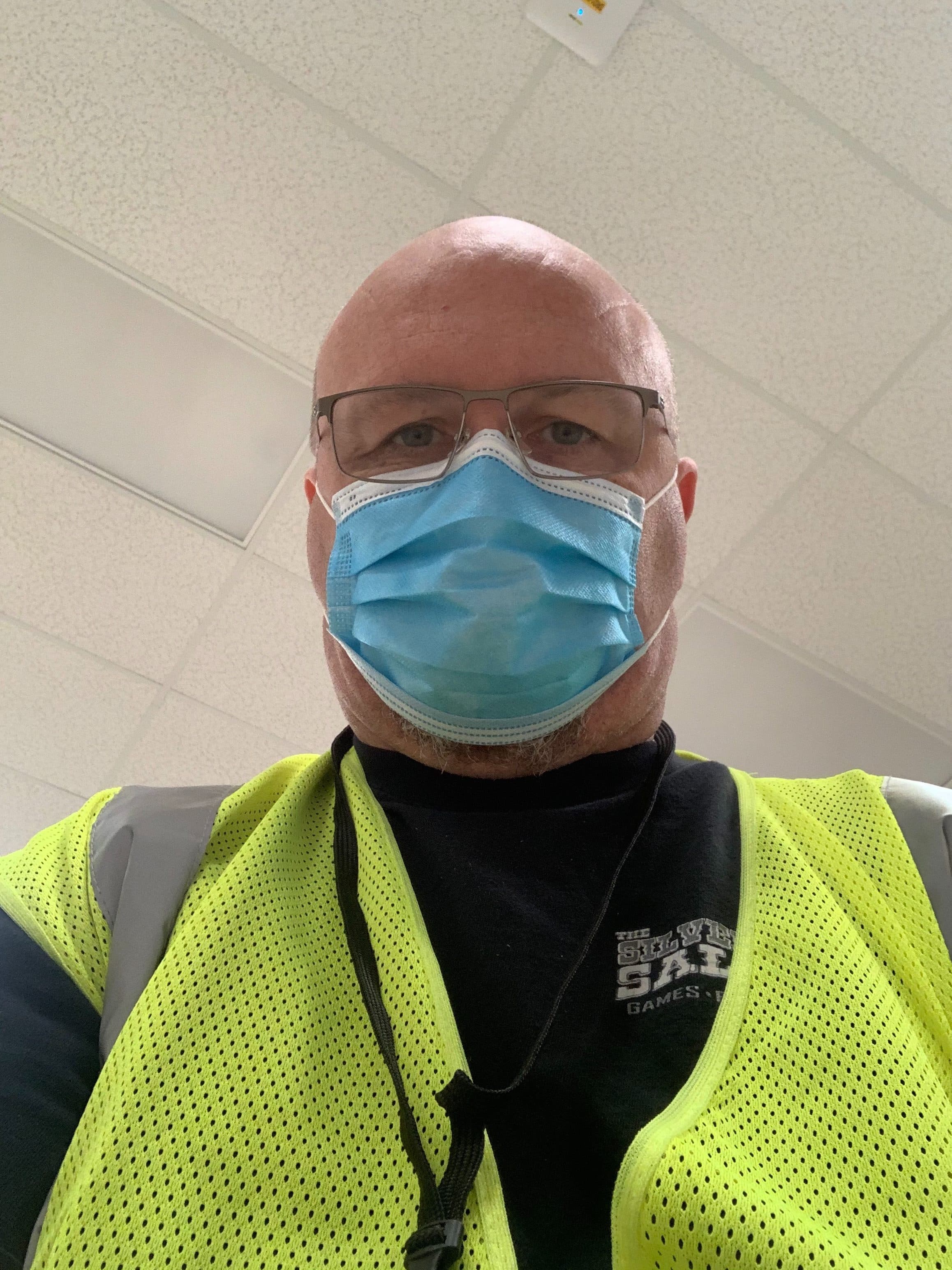 Bald person wearing glasses, mask, and bright yellow safety vest