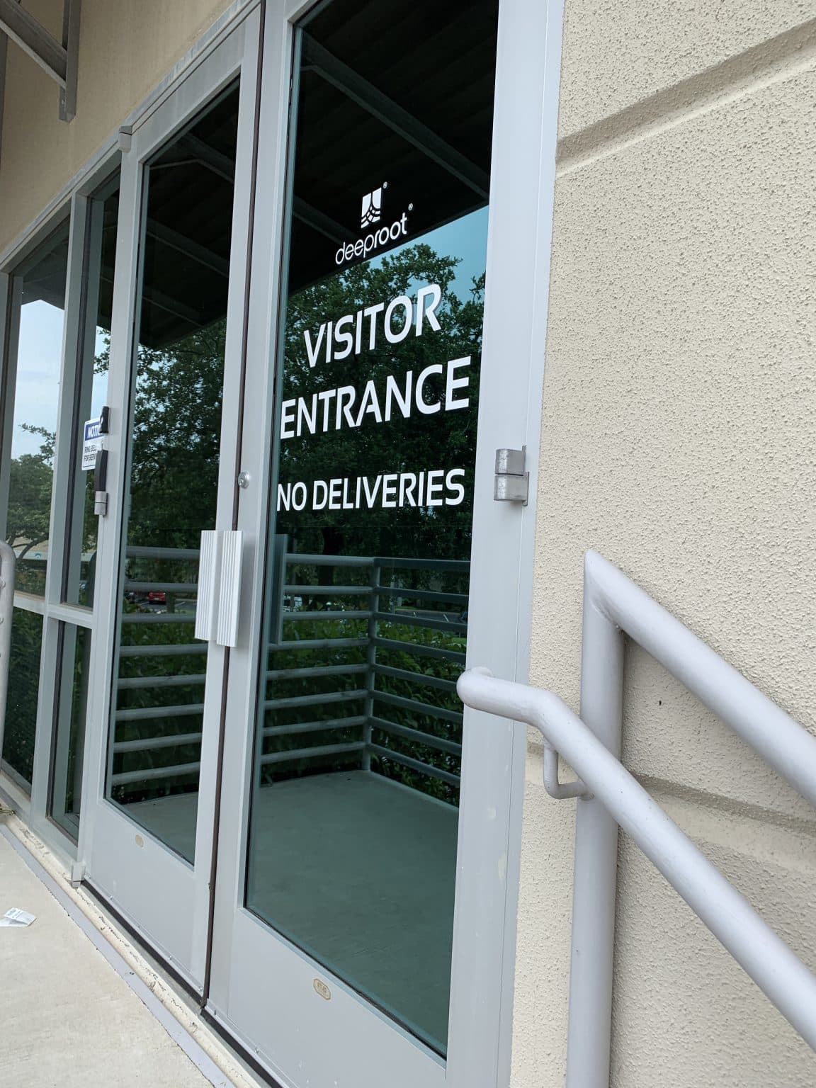 Deeproot visitor entrance door with "No Deliveries" sign and handrail