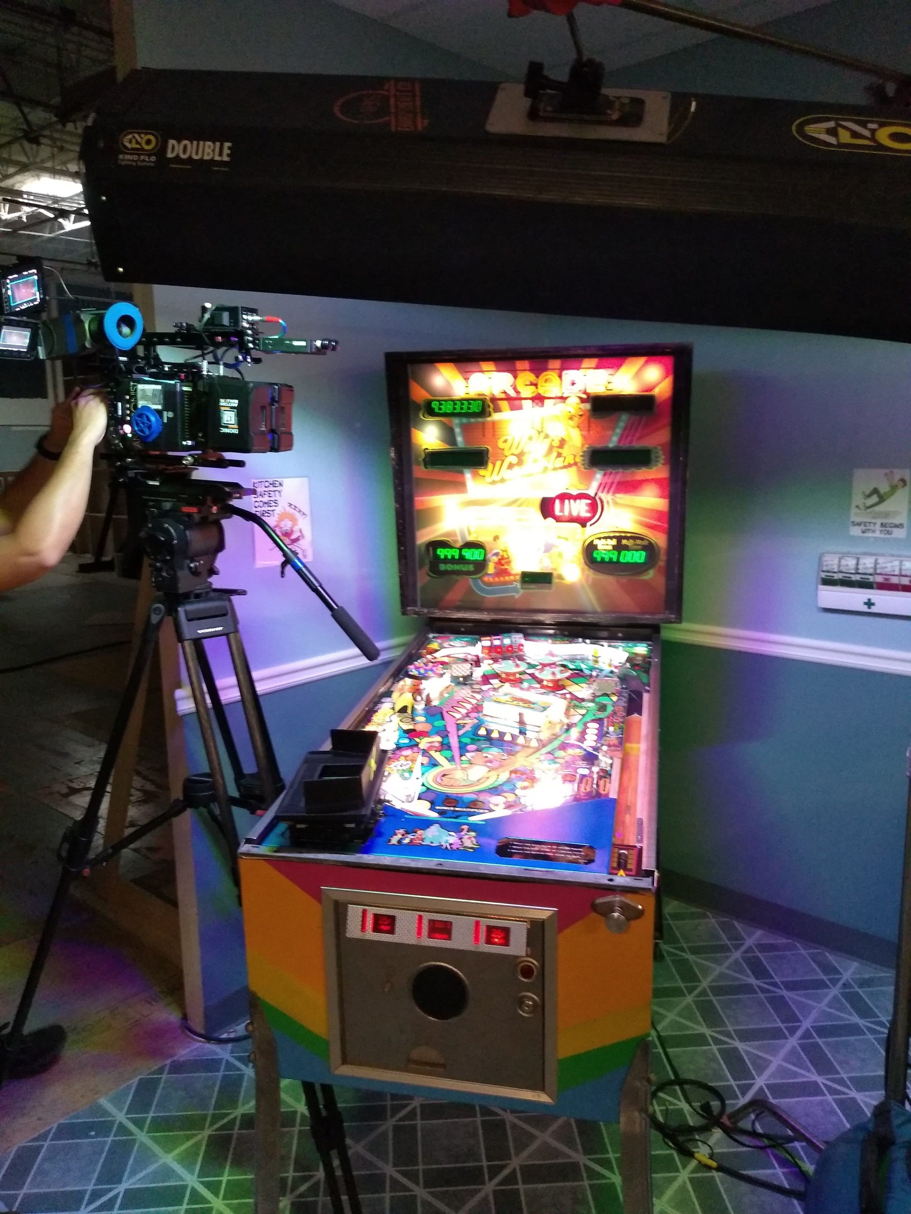 Colorful pinball machine with camera on tripod in arcade setting