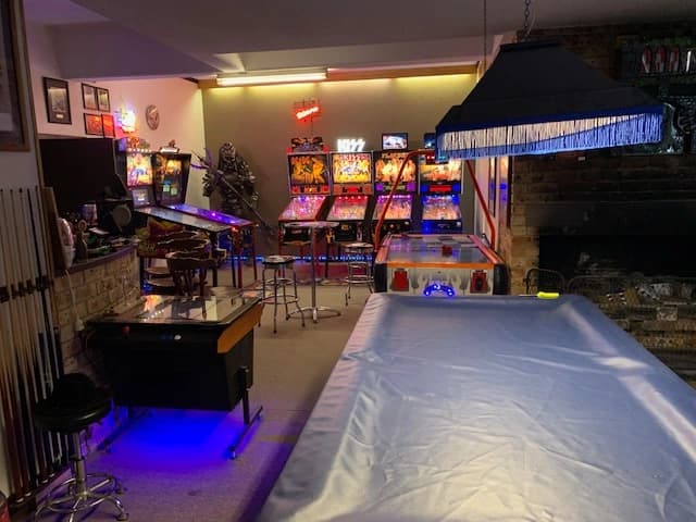 Game room with pinball machines, arcade games, and pool table lit with blue light