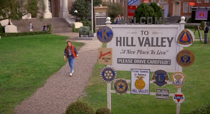 Welcome to Hill Valley sign with person walking on path near civic buildings