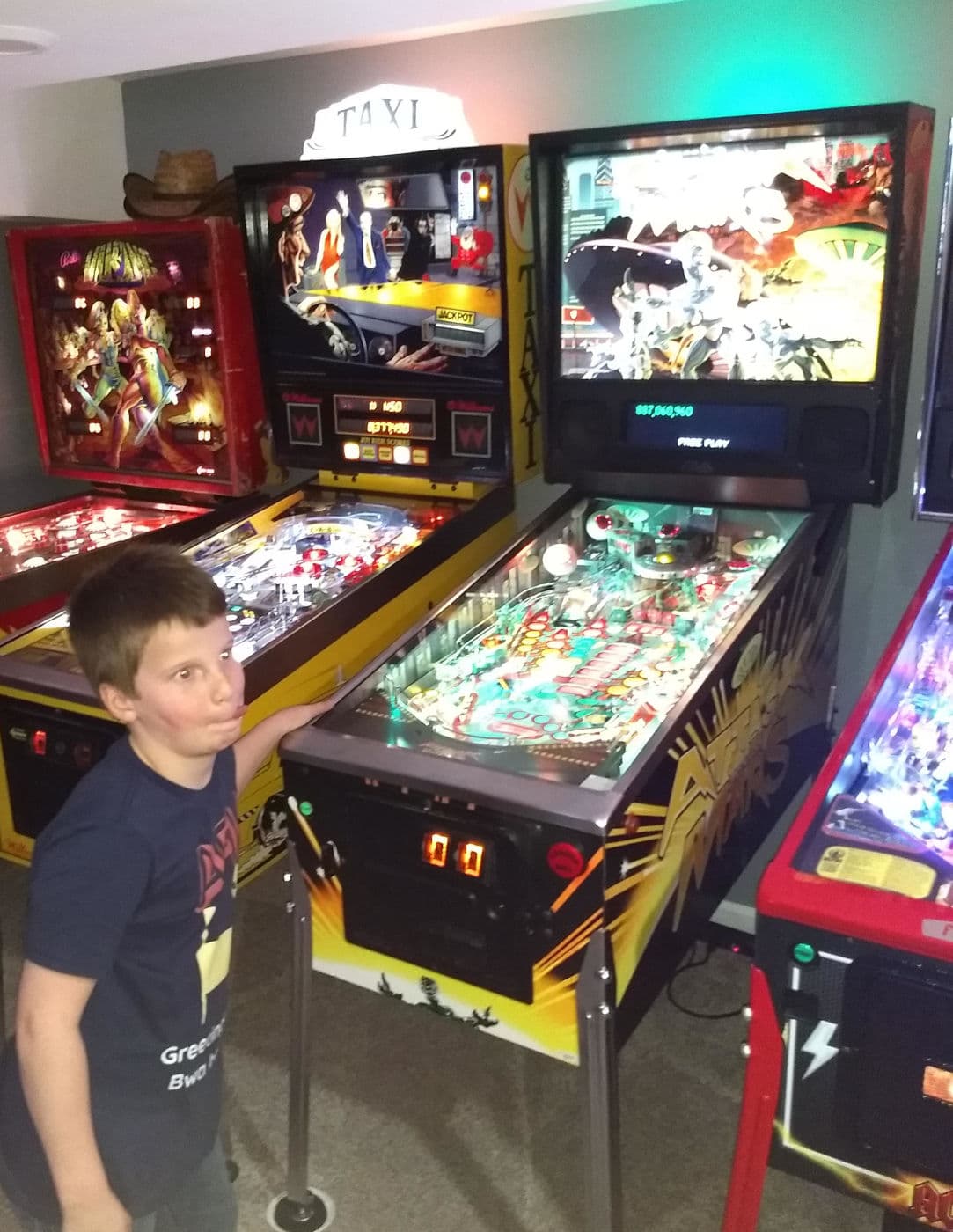 Young boy standing next to colorful vintage pinball machines in arcade