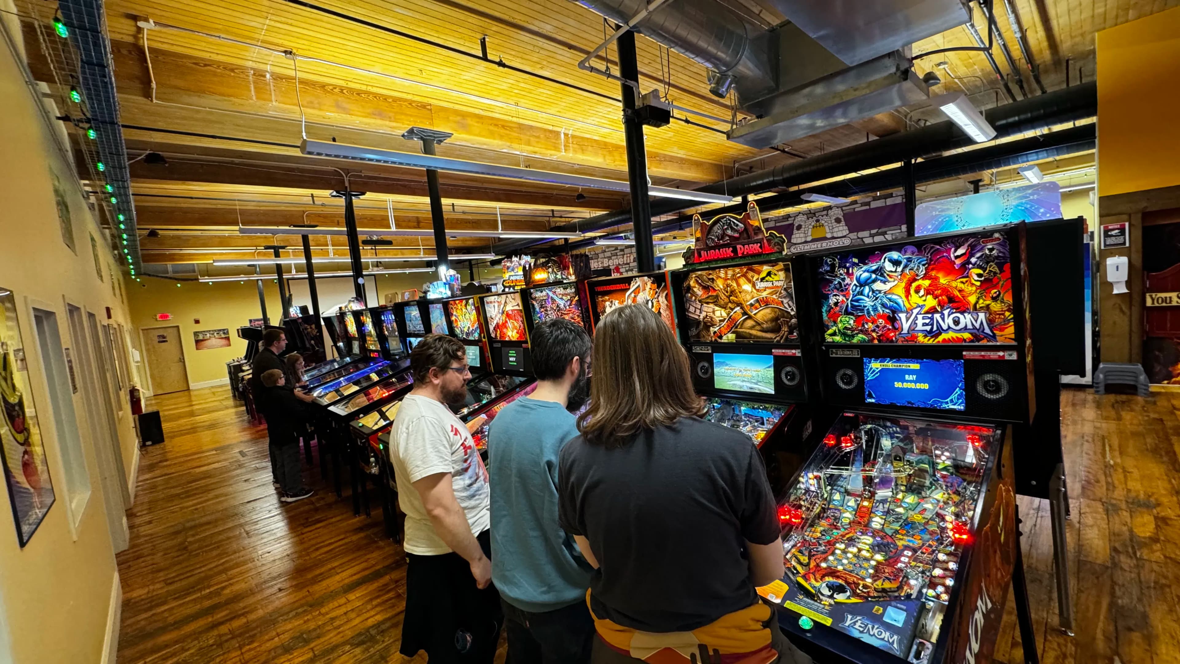 Pinball enthusiasts playing Venom and Jurassic Park machines in arcade