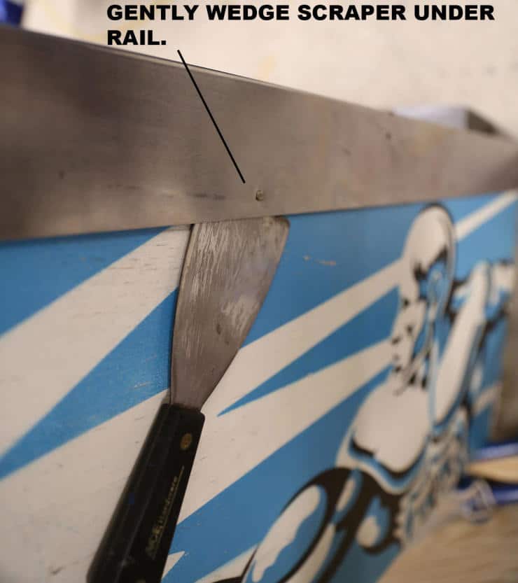 Scraper tool wedged under a metal rail on blue and white background