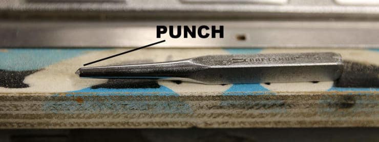 Metal punch tool with "PUNCH" label on textured workshop surface