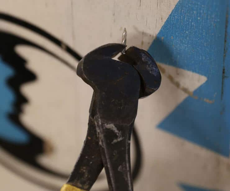 Rusty pliers with yellow handle gripping a nail against blue background