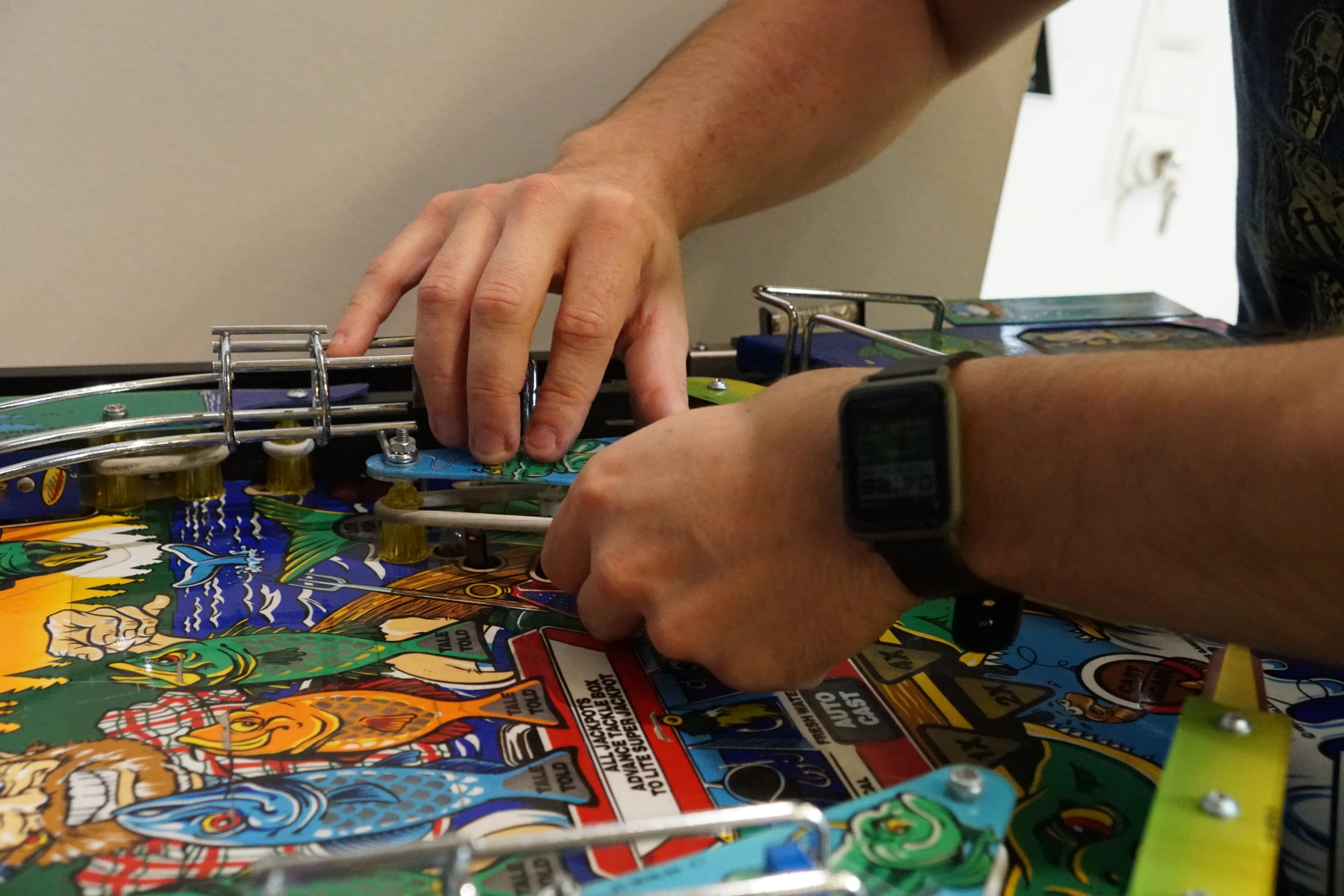 Hands adjusting colorful pinball machine with vibrant illustrated playfield