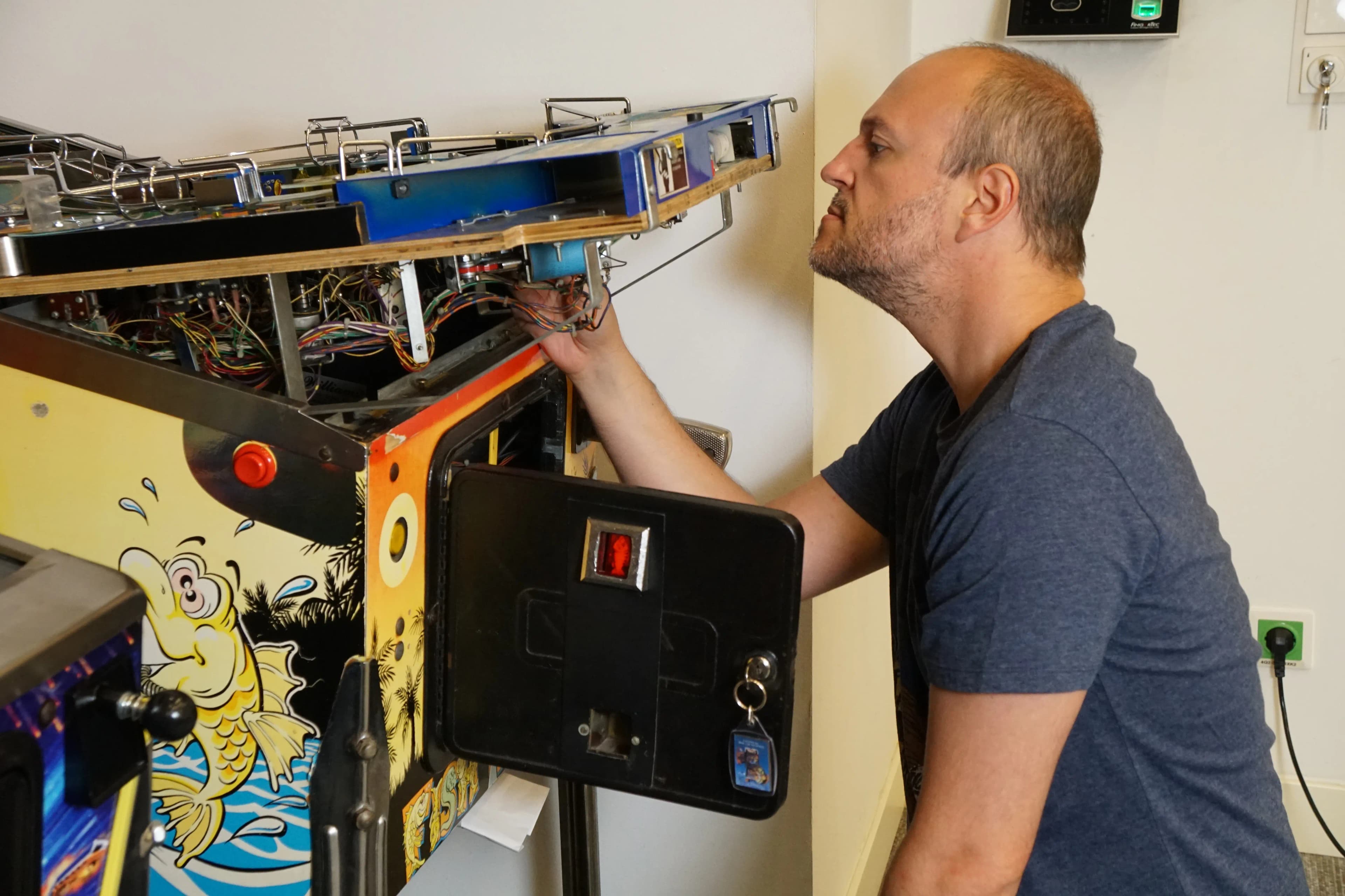 Technician repairing vintage arcade machine with colorful fish graphics